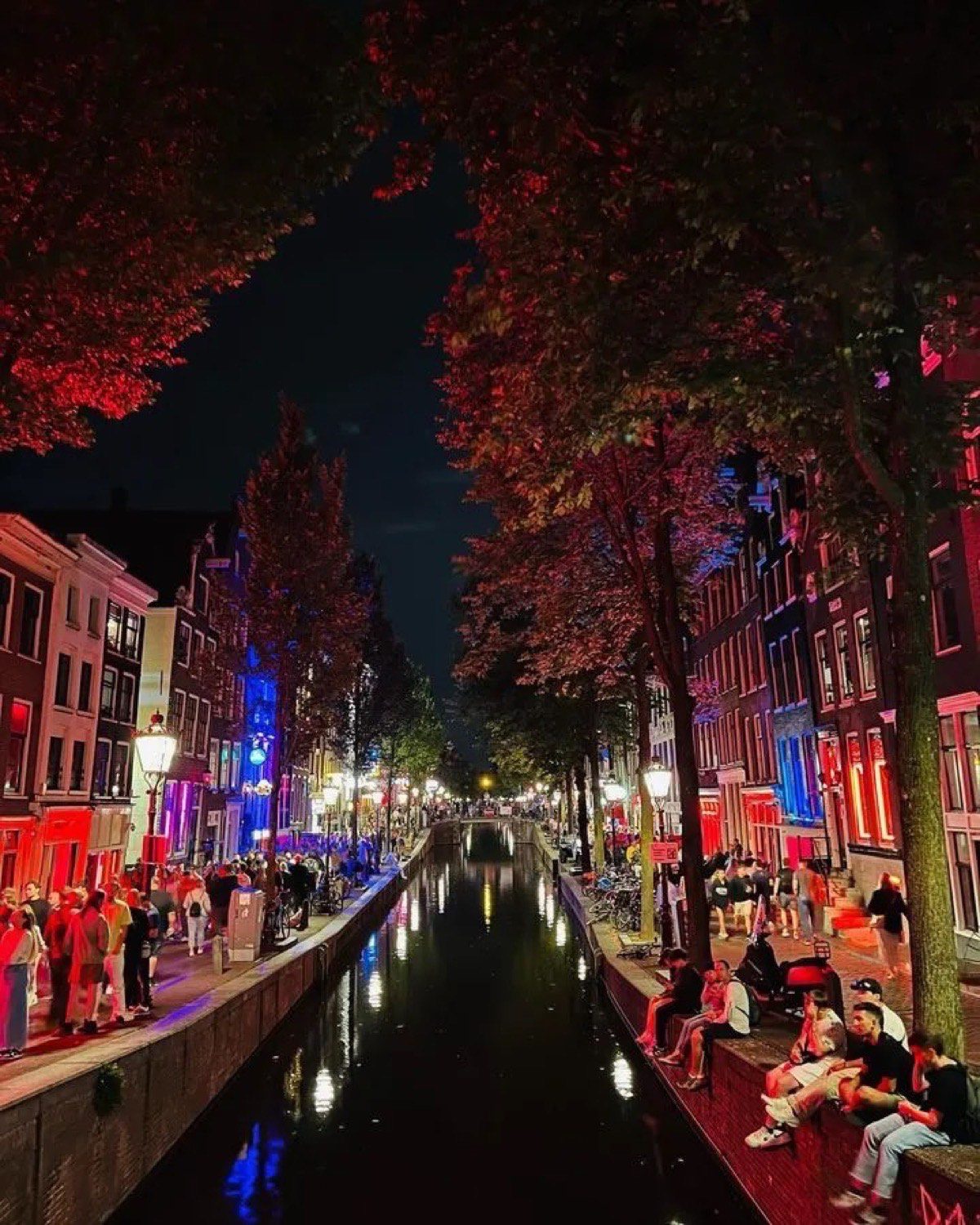 People beside a red-lit canal in De Wallen after dark.