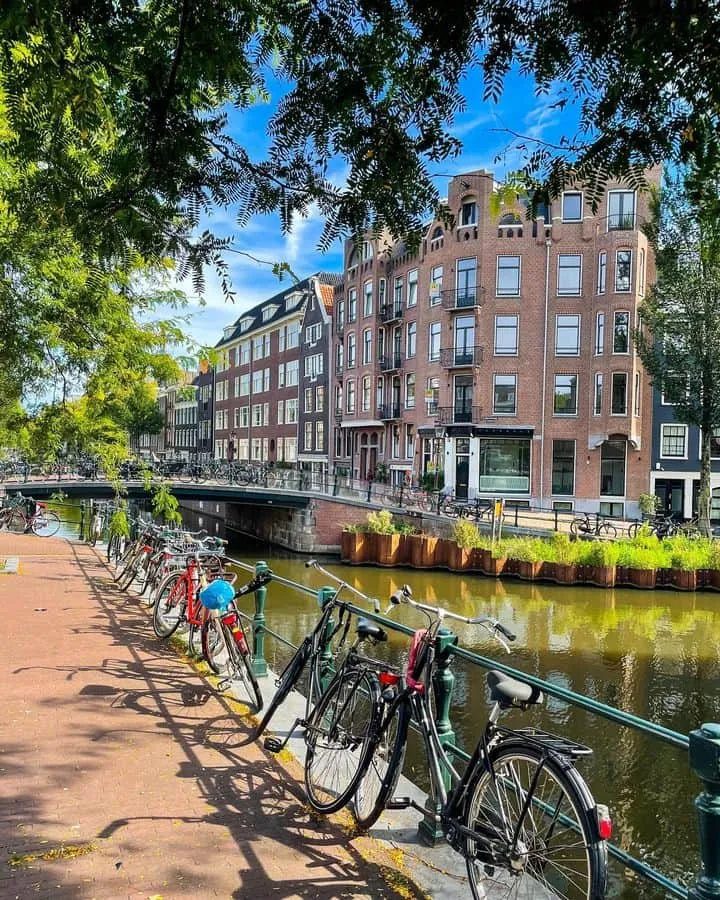 Bicycles against a canal railing in front of Jordaan brick houses.