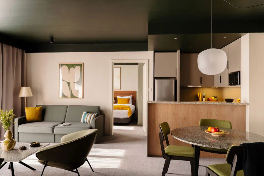 Sofa and a separate bedroom visible through a doorway in an Adina Budapest one-bedroom apartment.
