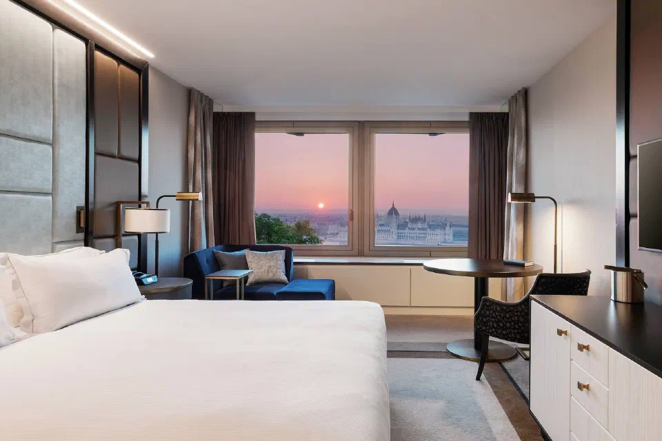 Bed and sitting area with Parliament visible through a Hilton Budapest room window.