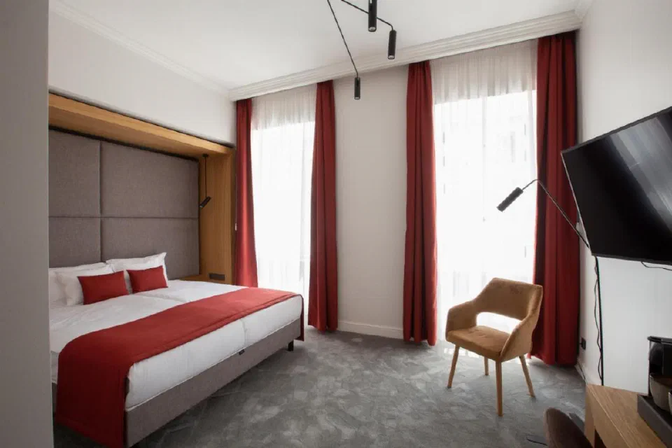 Bed with red accents beside tall windows at Monastery Boutique Hotel Budapest.