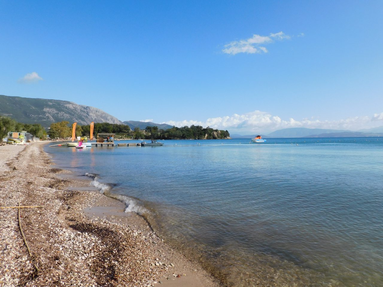 The pebbled shoreline and calm bay at Dassia, with green hills beyond.