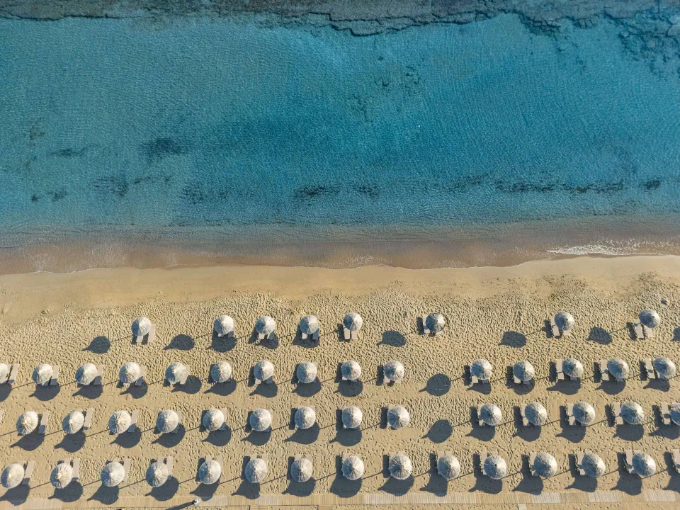 Overhead view of sandy beach, rows of parasols and turquoise water at Agapi Beach Resort.