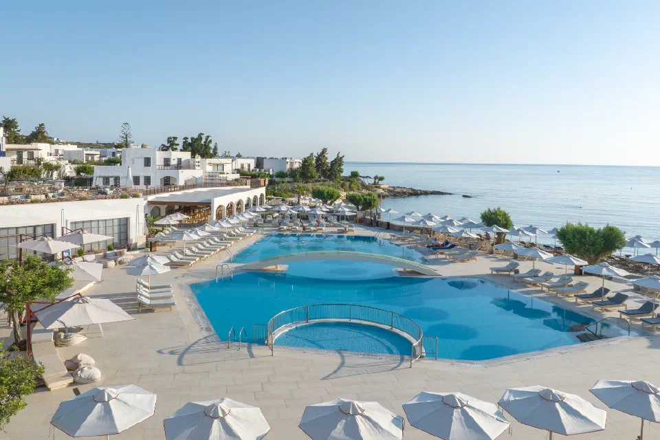 An outdoor pool, sun terraces, white resort buildings and the sea at Creta Maris.
