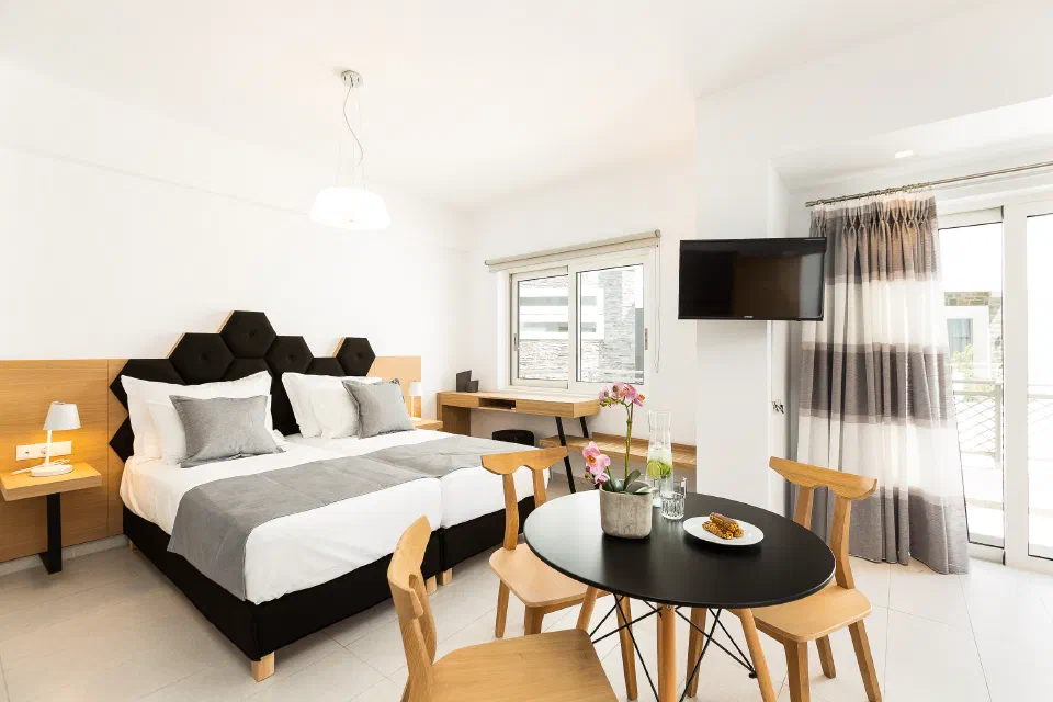 A bright Cyano Hotel room with a double bed, dining table and balcony doors.