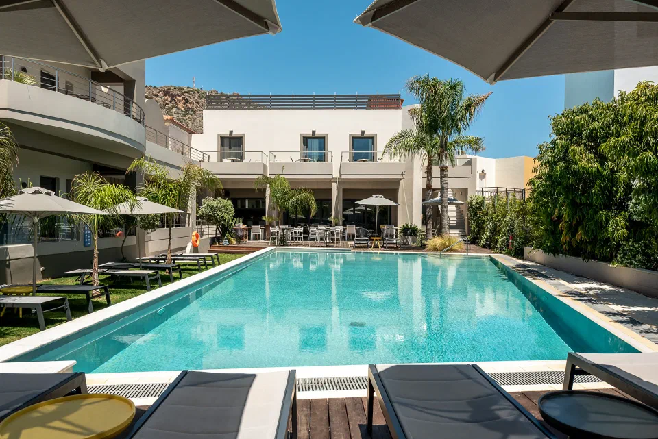 Outdoor pool with loungers, palms and hotel balconies at Libyan Princess in Paleochora.