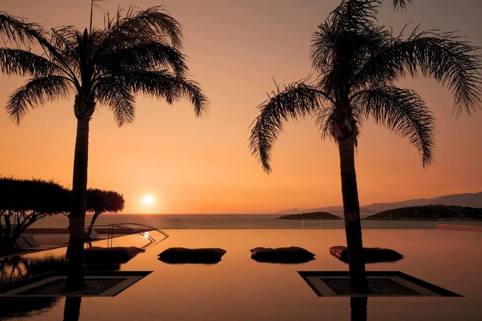 Sunrise over the infinity pool and palms at Minos Palace Resort.