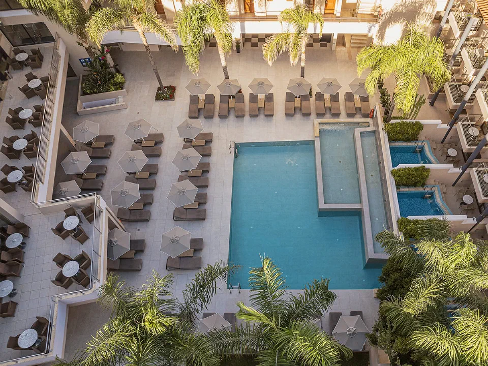 Aerial view of a turquoise pool, loungers, palms and guest-room wings at Porto Platanias.