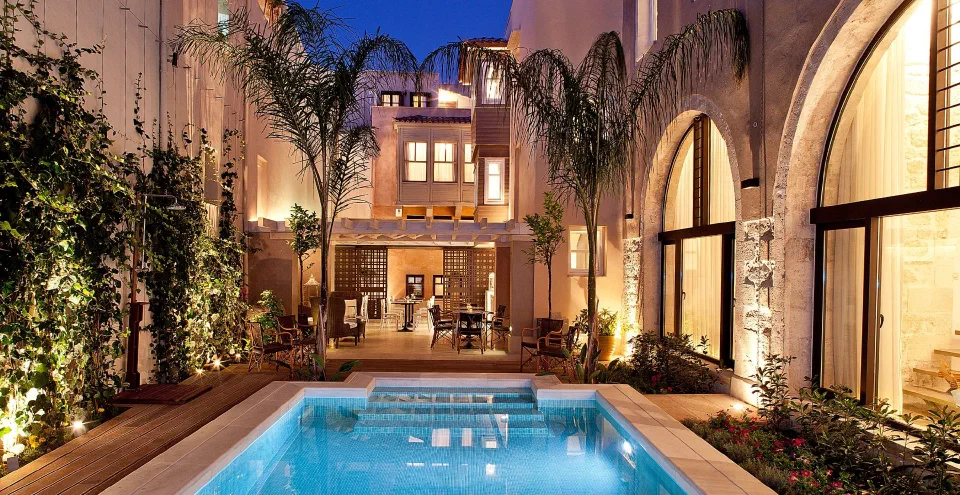 An illuminated courtyard pool with palms and stone archways at Rimondi Boutique Hotel.