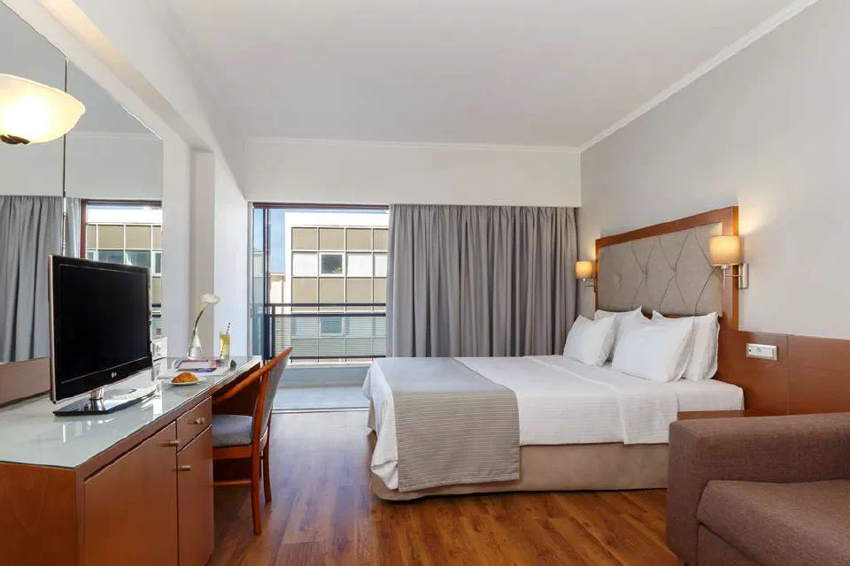 Guest room with a bed, desk, armchair and balcony doors at Best Western Plus Hotel Plaza in Rhodes.