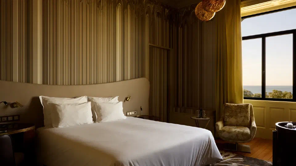 A white bed, striped wall panels and an Atlantic-facing window in a Manor House Ocean Front Room at Vila Foz.