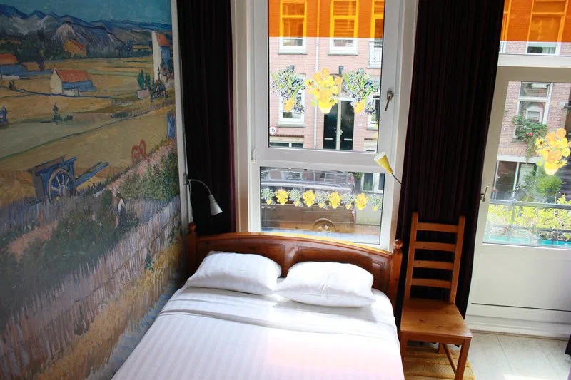 A simple double bedroom at Bicycle Hotel with a Van Gogh-style mural and a bright window.