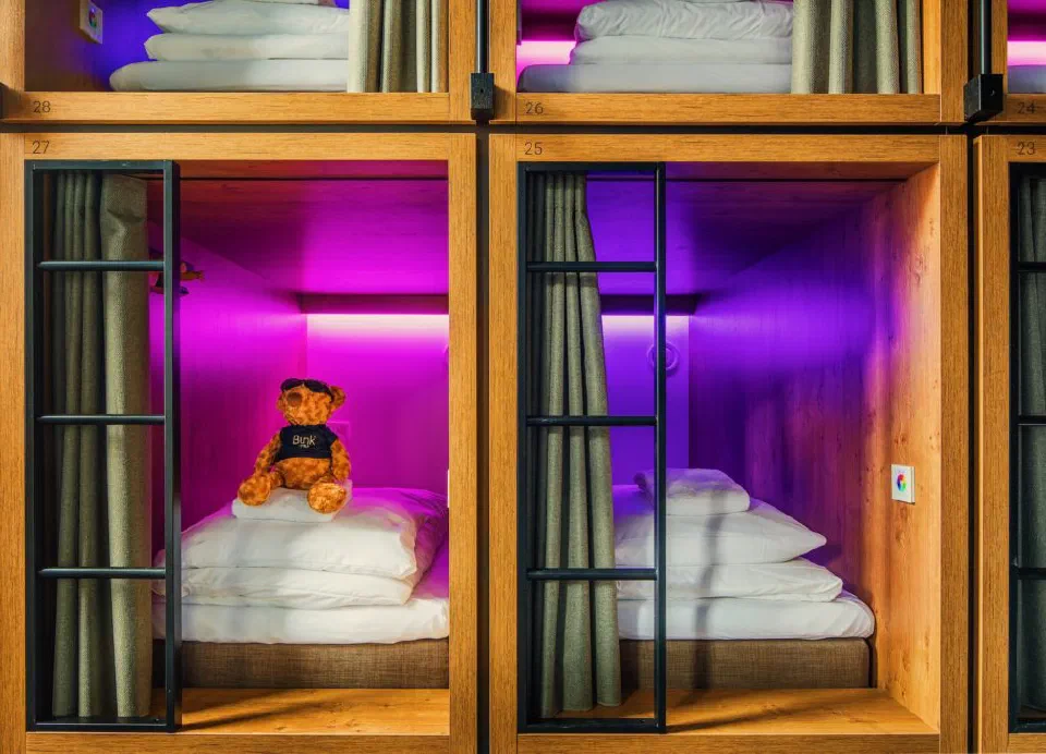 Stacked sleeping pods at Bunk Amsterdam with curtains, ladders and coloured lighting.