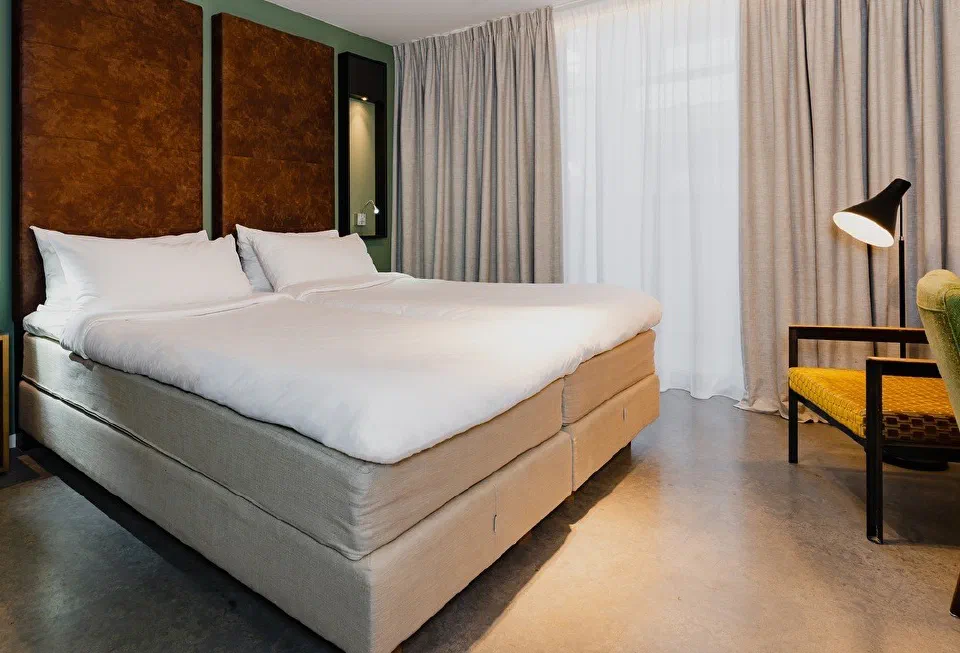 A Comfort Room at Hotel De Hallen, with a broad bed, warm headboards and a yellow-green armchair.