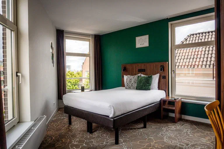 A Superior Double at Linden Hotel, with a green wall, double bed and windows around the angled room.