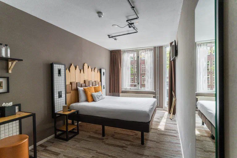 A bedroom at Mr. Jordaan with a timber headboard, mustard cushions and tall windows.