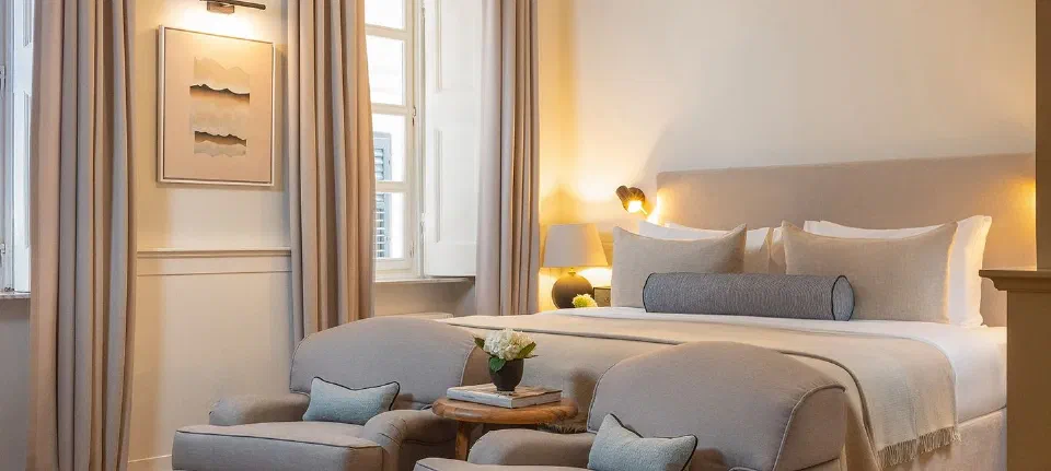 Neutral-toned bedroom with tall windows and a sitting area at Boutique Hotel Stari Grad.