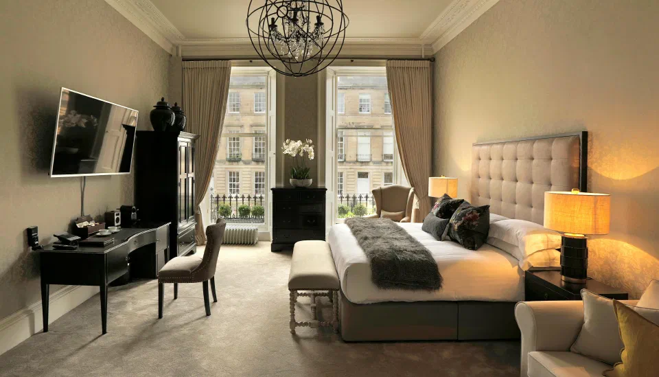 Tall windows, a chandelier and an upholstered bed in a Junior Suite at Nira Caledonia.