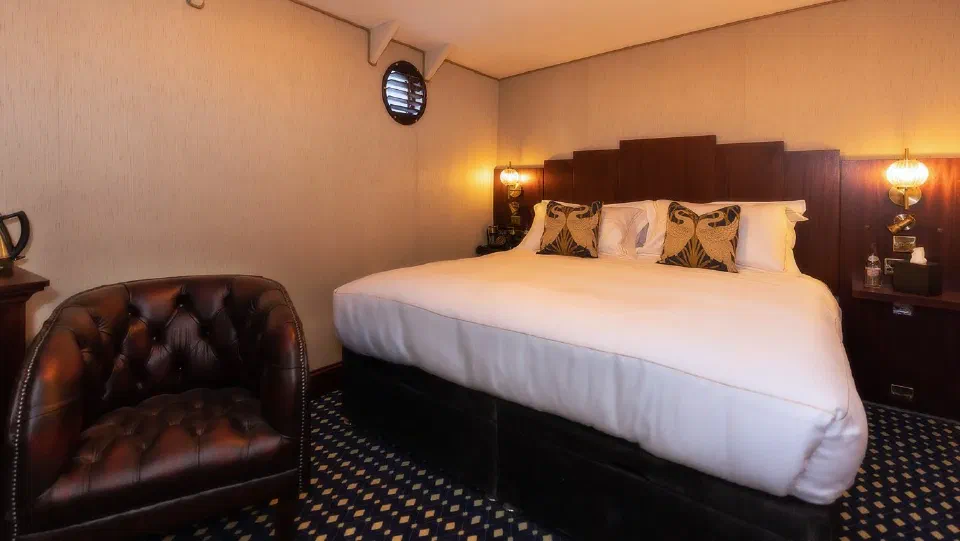 Double bed, leather armchair and porthole in a Standard Cabin aboard Ocean Mist Leith.
