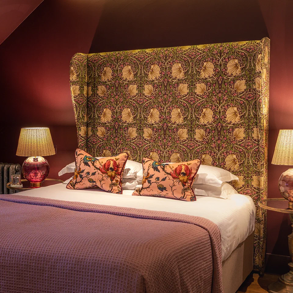 Patterned headboard and warm bedside lamps in a bedroom at The Raeburn.