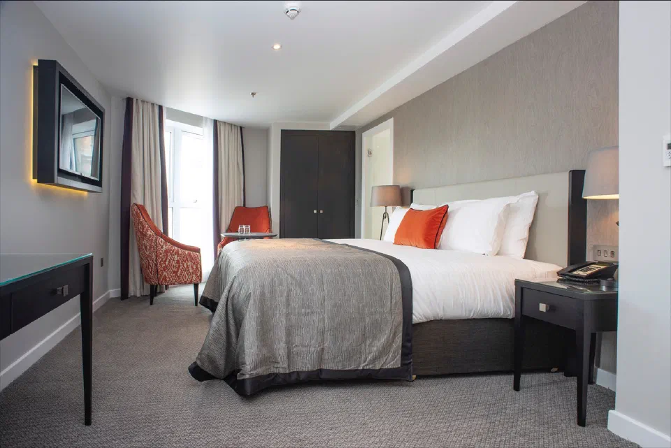 Double bed with orange cushions and a window-side seating area in a Superior Room at Ten Hill Place.