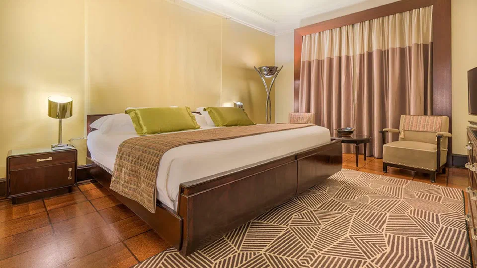 Art Deco-style bedroom at Hotel Britania, with timber furniture and a geometric rug.