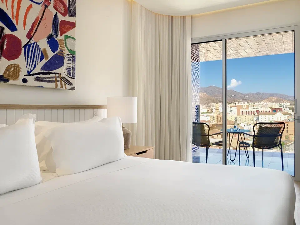 White bed and furnished terrace in a Superior room at H10 Croma Málaga.