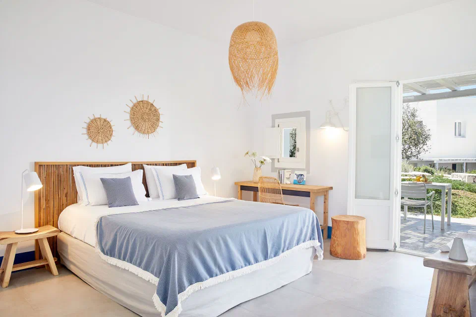 White double bedroom with blue textiles and an open terrace doorway at Milos Breeze.