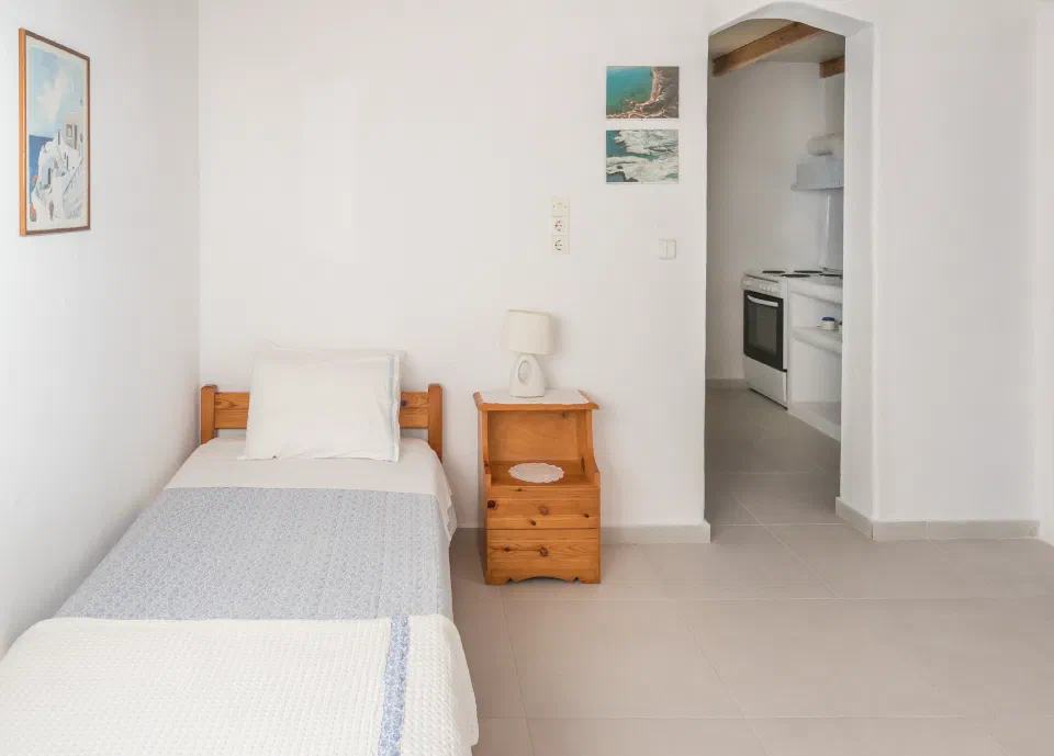 Single bed and bedside table beside an open doorway to the kitchen in a Sarantis One-Bedroom Apartment.