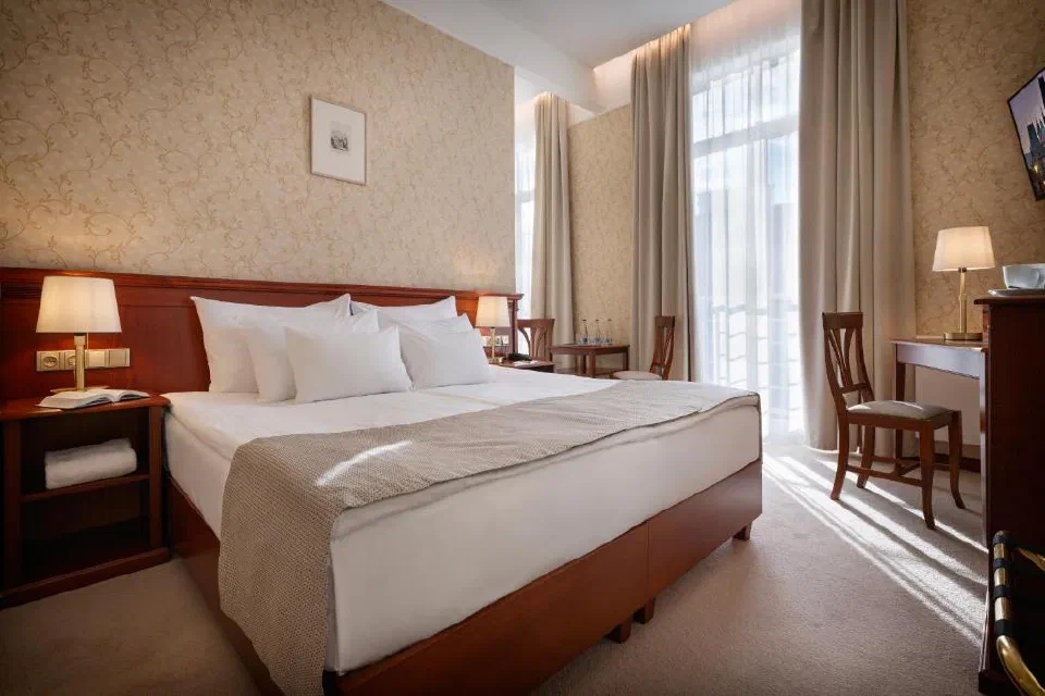 Guest room at Hotel Rott with a wooden double bed and tall windows.