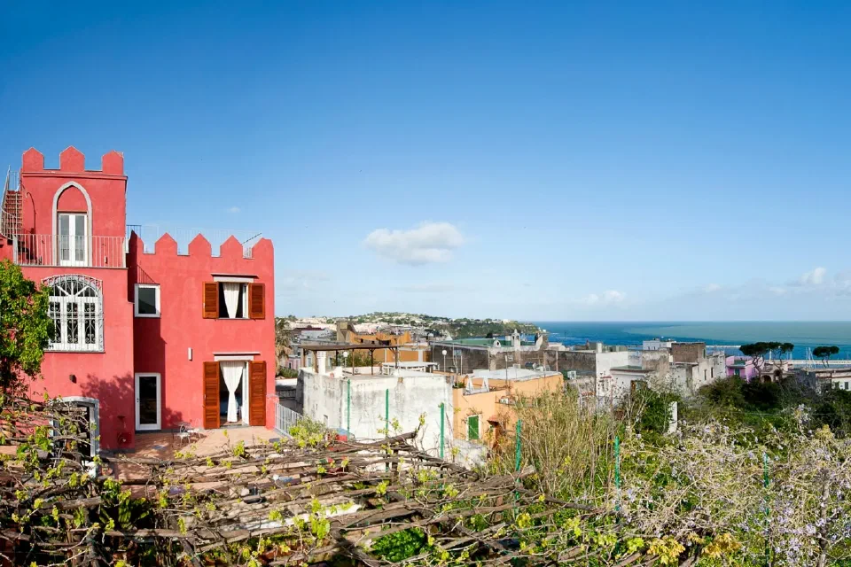 Hotel La Vigna’s red tower beside its garden and vineyard, with Procida and the sea beyond