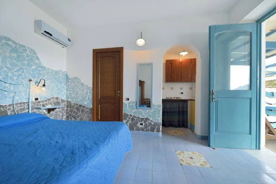 Azzurromare apartment interior with a blue bed, kitchenette and open terrace door
