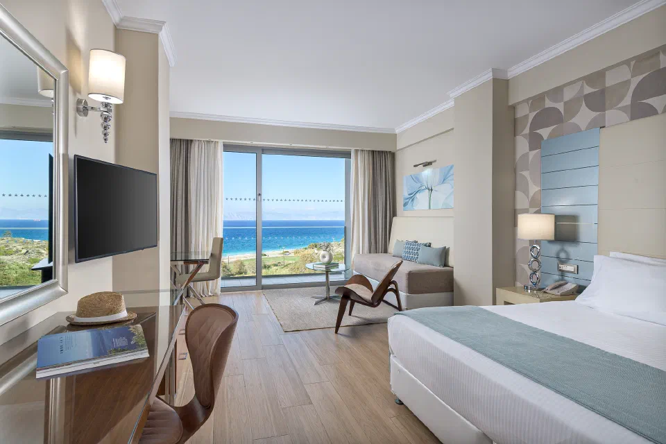 Bed and seating area facing a sea-view balcony in an Atrium Platinum Deluxe Room Sea View.