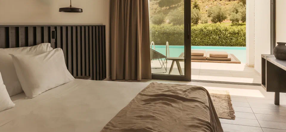 Bed beside sliding doors opening onto a terrace and shared pool at Casa Cook Rhodes.