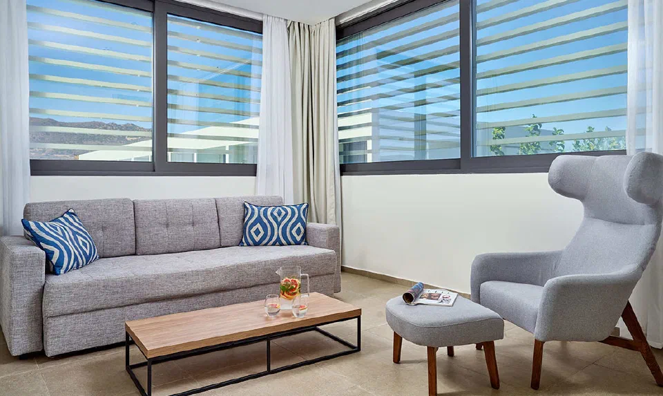 Sofa and armchair beside wide shaded windows in a Suite Sea View at Gennadi Grand Resort.