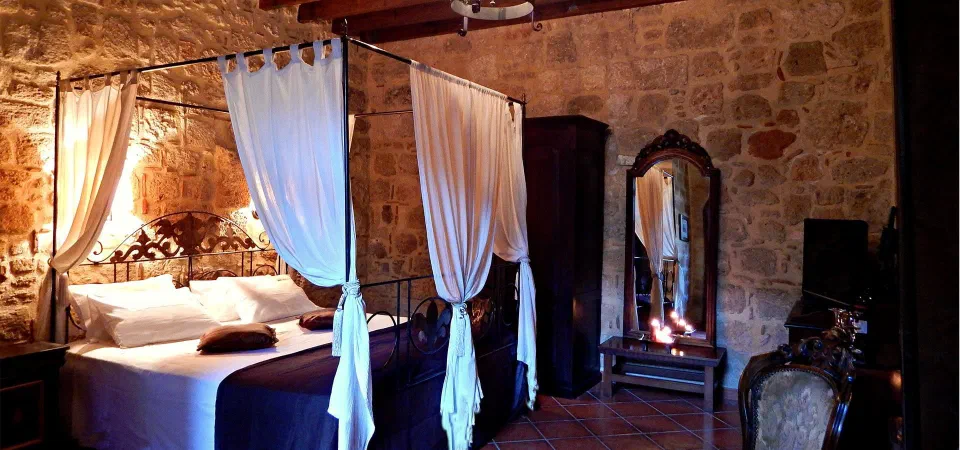 Draped four-poster bed in a stone-walled Medieval Room at S. Nikolis Historic Boutique Hotel.