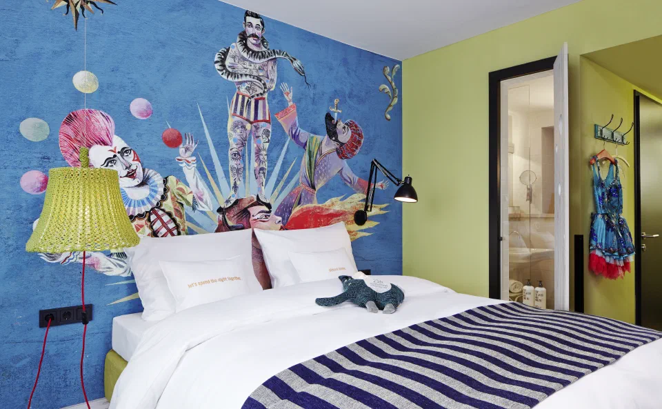 A colourful Medium room at 25hours Hotel beim MuseumsQuartier, with circus mural, white bed and playful details.