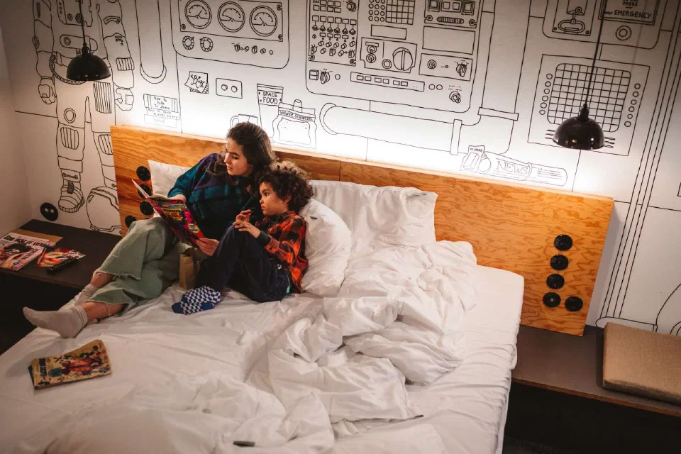 A parent and child reading together on a bed in Superbude Wien Prater's family-room setting.