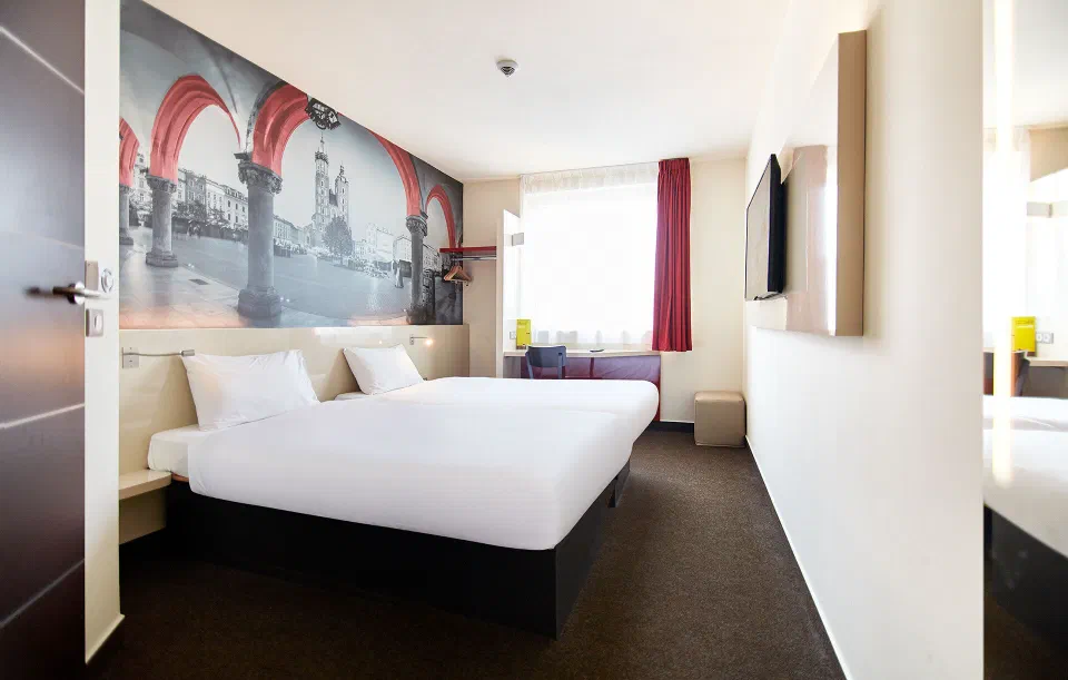 Two single beds beneath a Kraków mural in a bright room at B&B HOTEL Krakow Centrum.