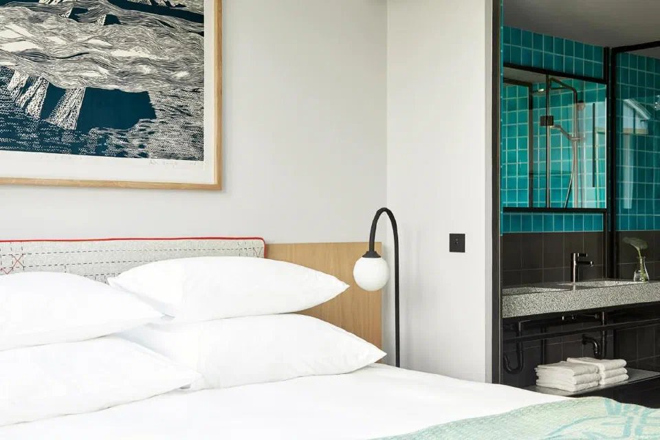 White bed, graphic artwork and a turquoise-tiled bathroom at PURO Kraków Kazimierz.