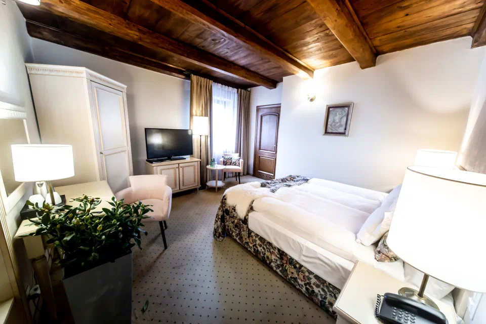 Wood-beamed ceiling, a double bed and a seating corner in a Standard Room at Hotel Rubinstein.