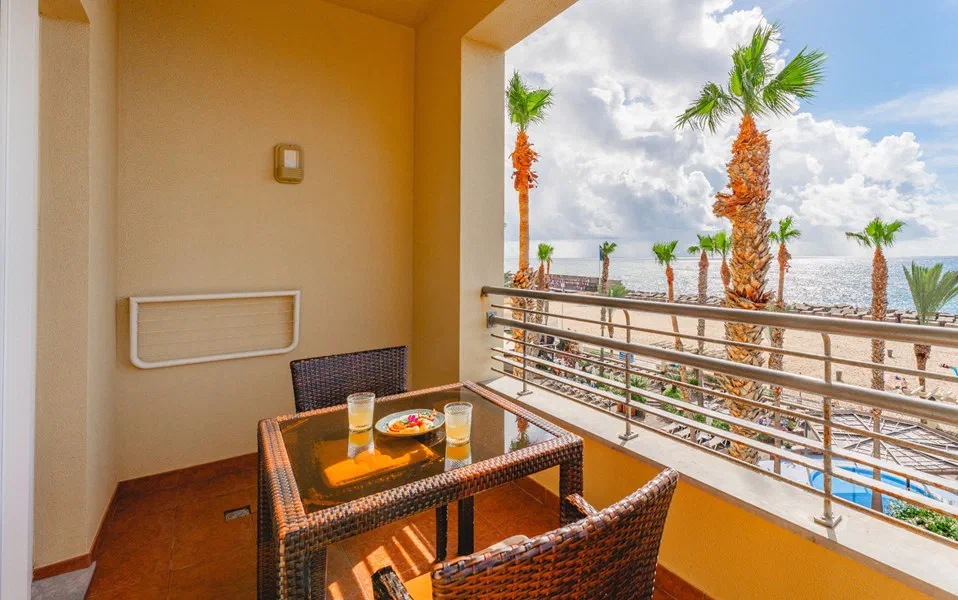 A Double Sea View room balcony at Calheta Beach, overlooking palms, the pool and ocean.