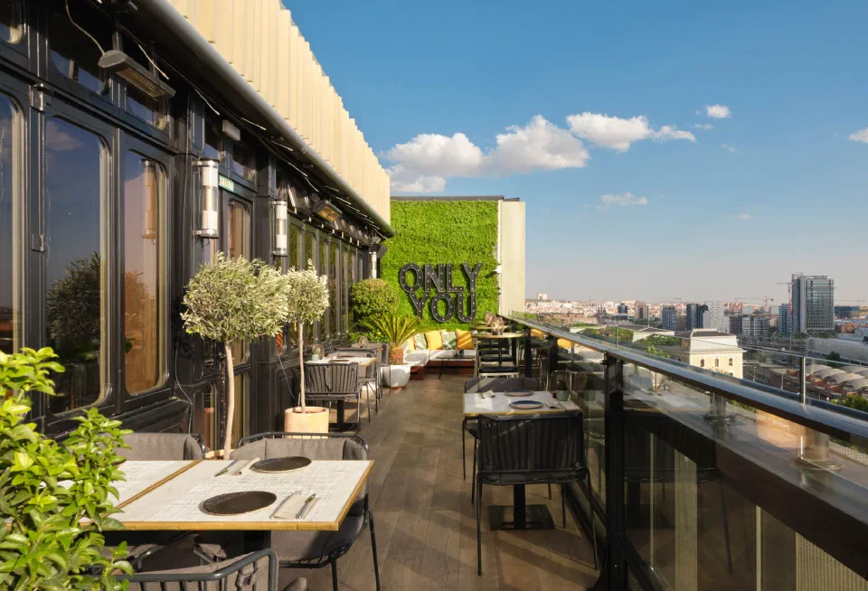 Open-air rooftop terrace at Only YOU Hotel Atocha, with dining tables, greenery and Madrid skyline views.