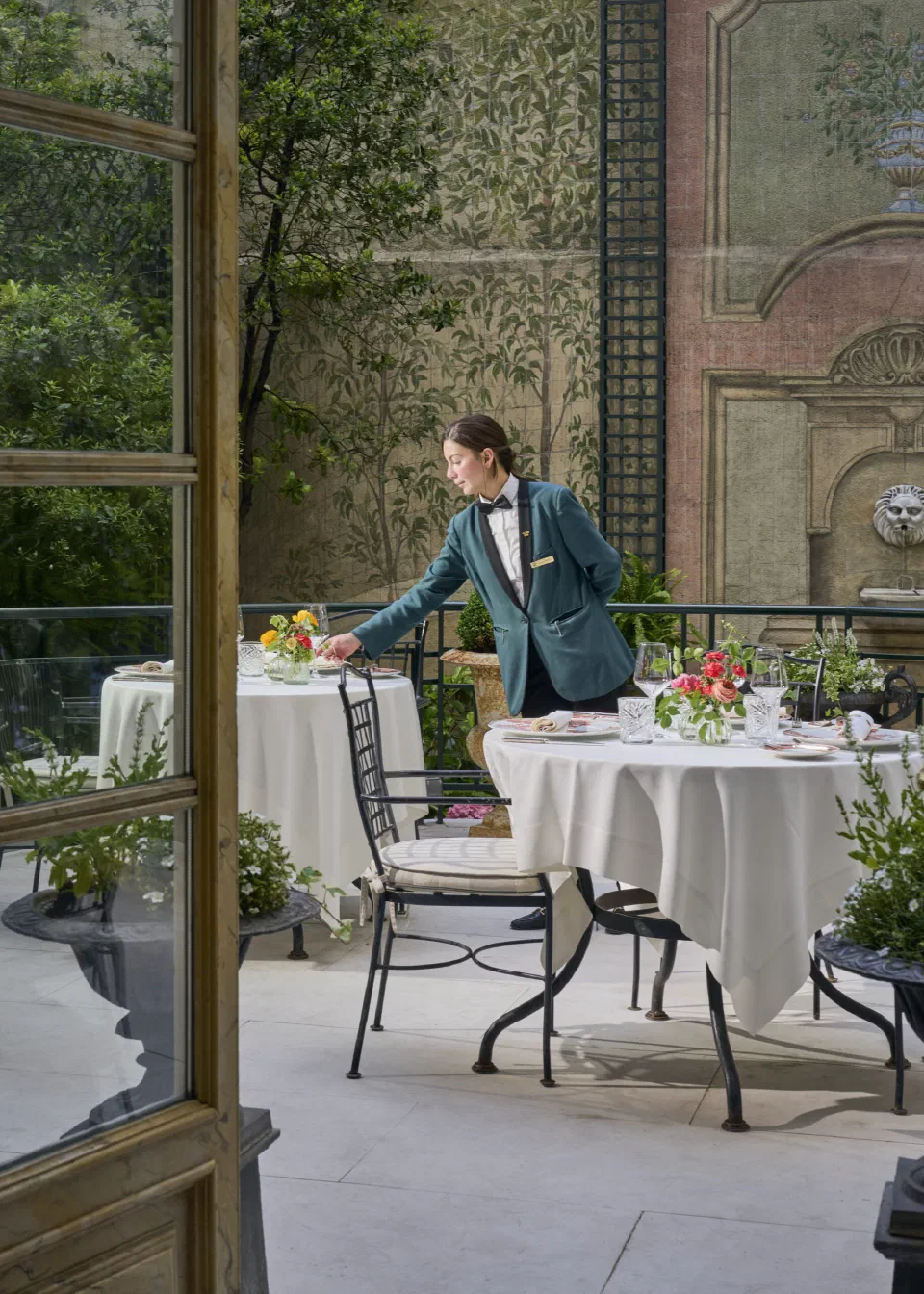 Tables set among plants in Hotel Orfila's garden courtyard, with a staff member arranging flowers.