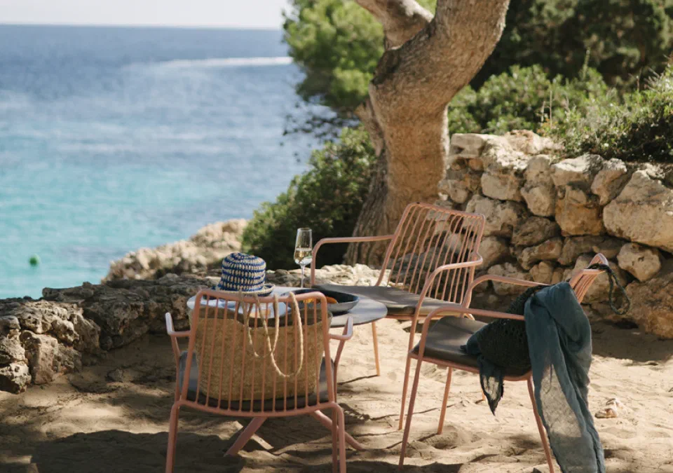 Terrace chairs beneath pine trees at Inturotel Cala Esmeralda, overlooking the sea.