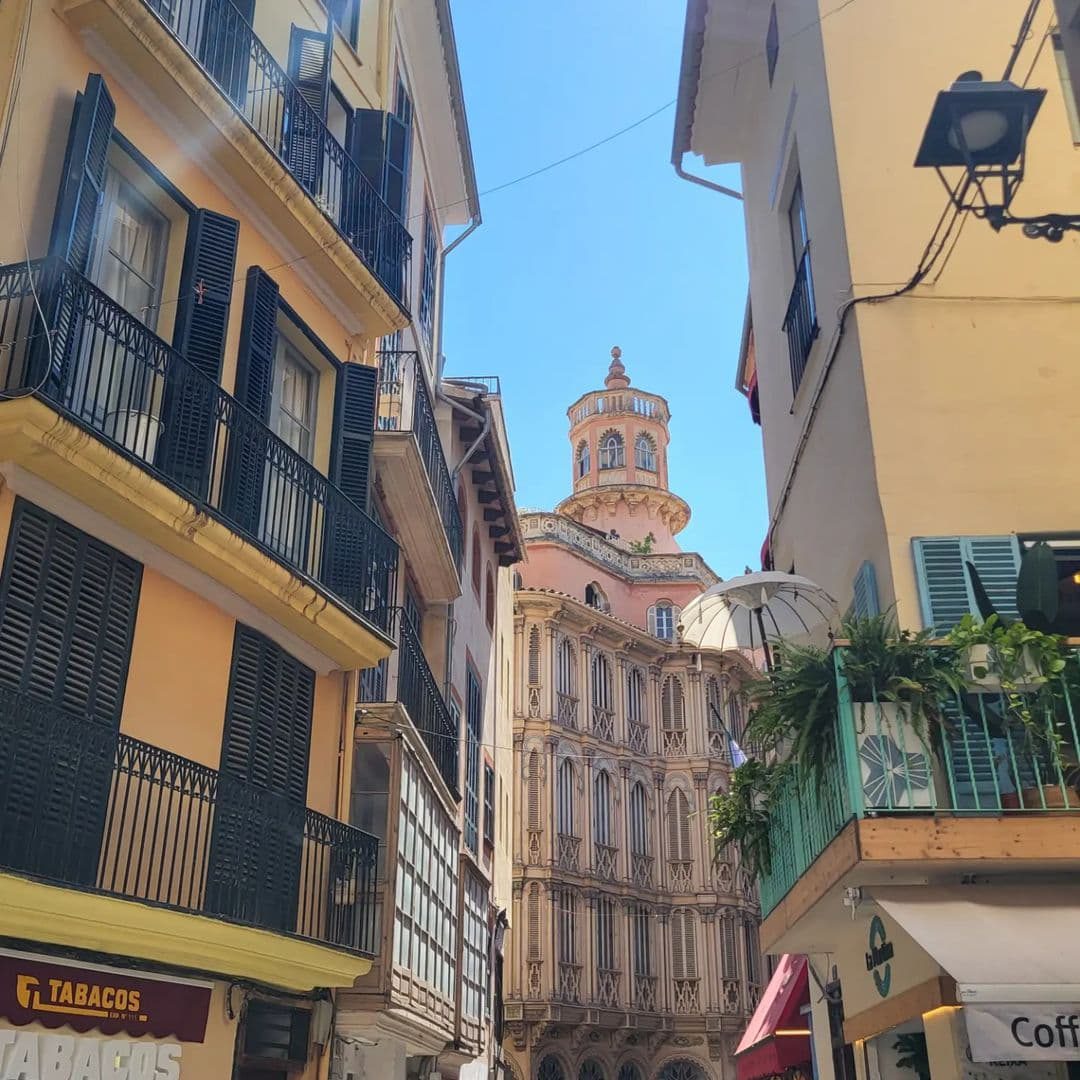 A narrow Palma old-town street with balconies and a church tower beyond.