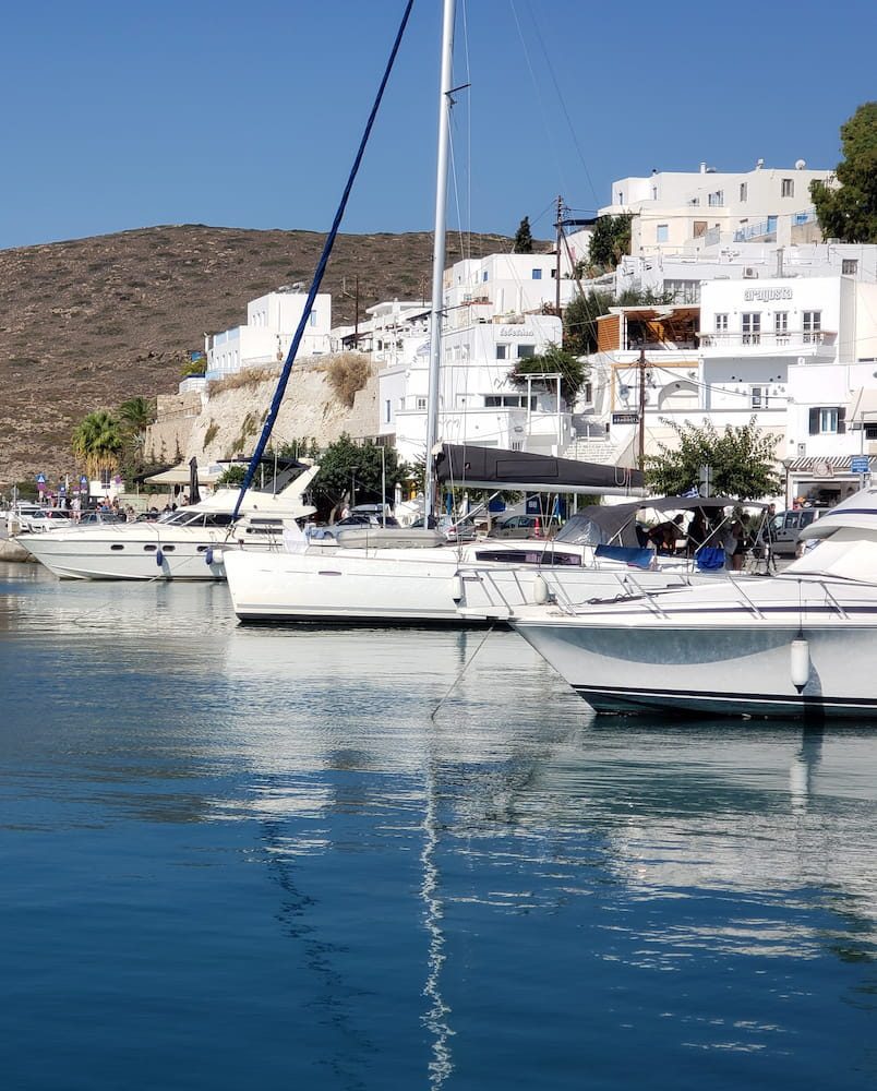 Boats beside the Adamas waterfront and white houses on the hill.