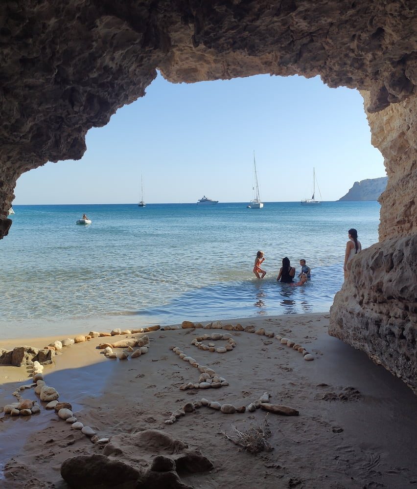 Boats and swimmers in a southern Milos cove, viewed through a rocky opening.