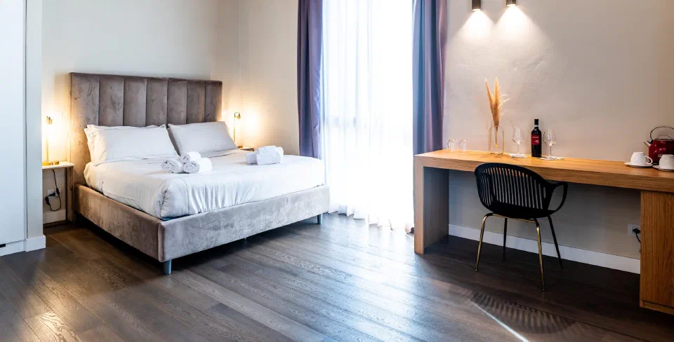 Double bed and wooden desk beside a tall window in a Superior room at Bastione Spasimo, Palermo.