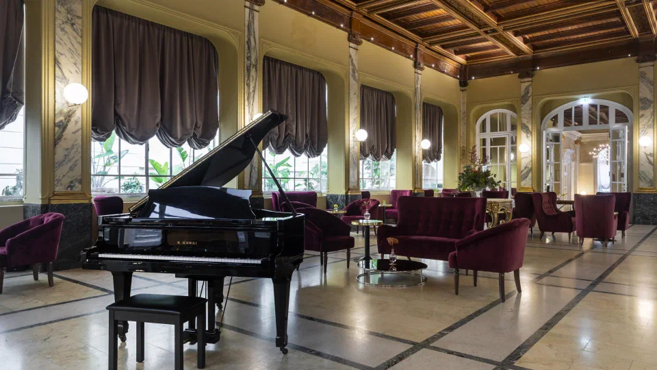 Grand piano and burgundy seating in the winter garden lounge at Grand Hotel et Des Palmes, Palermo.